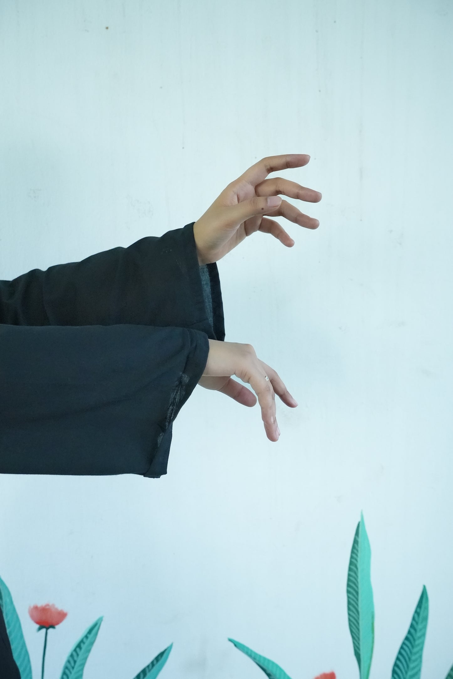 Person wearing a dark jacket with a light background and plant designs. Karaa