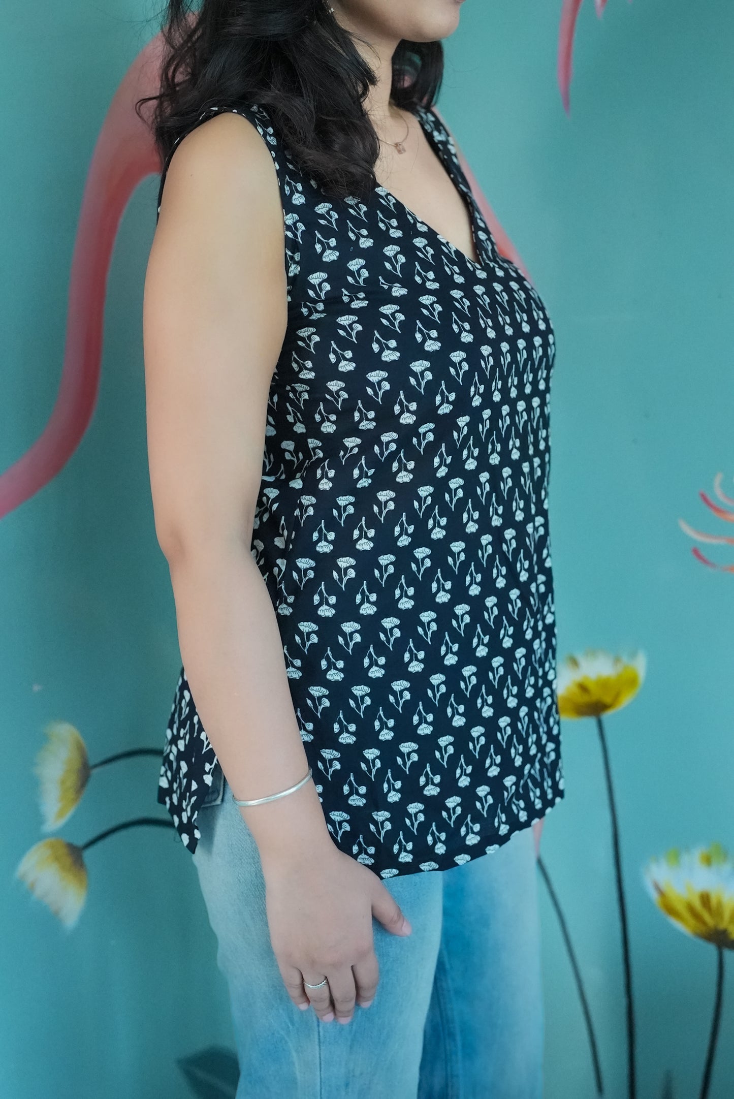 Woman wearing a black sleeveless top with white floral pattern against a colorful background Karaa