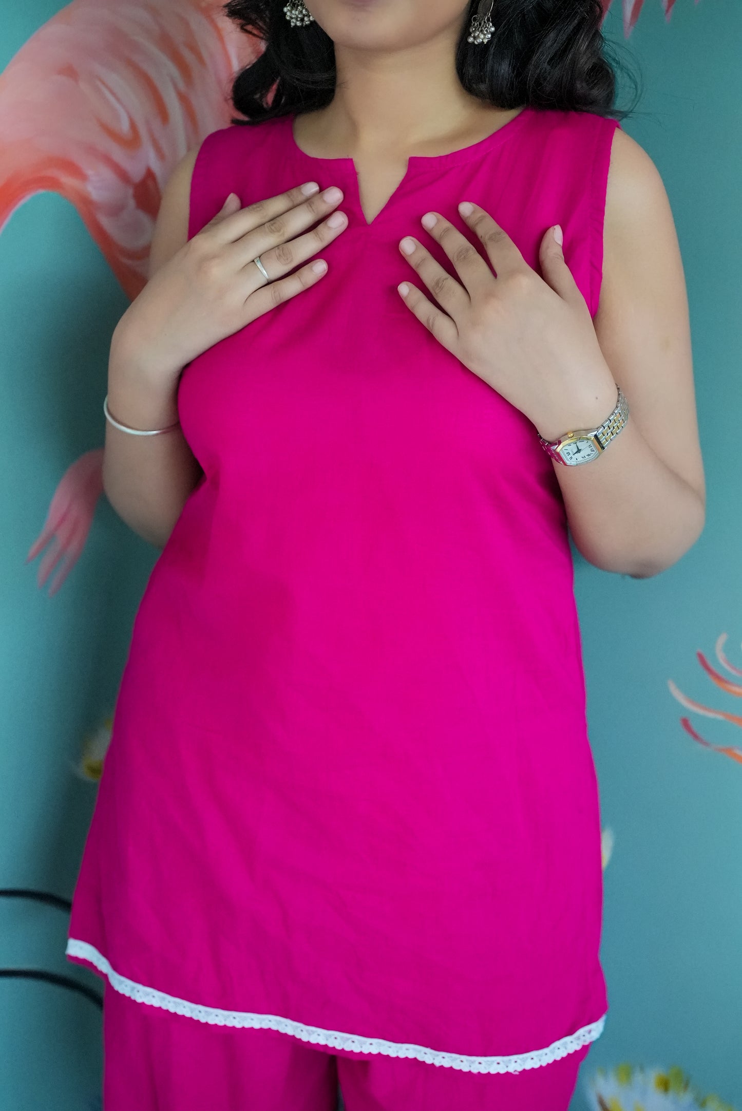 Woman wearing a bright pink dress with white trim against a teal background Karaa