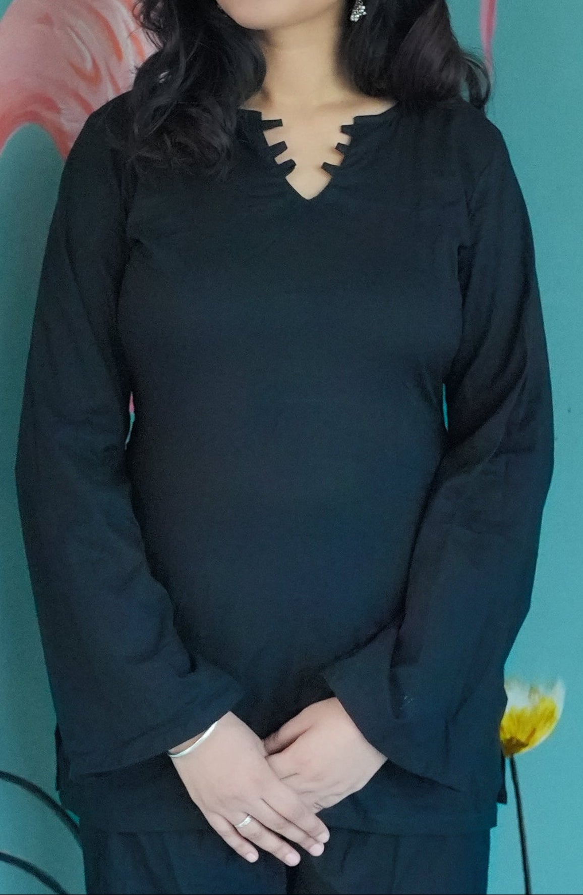 Woman in a black outfit standing in front of a teal wall with pink flamingo illustrations. karaa