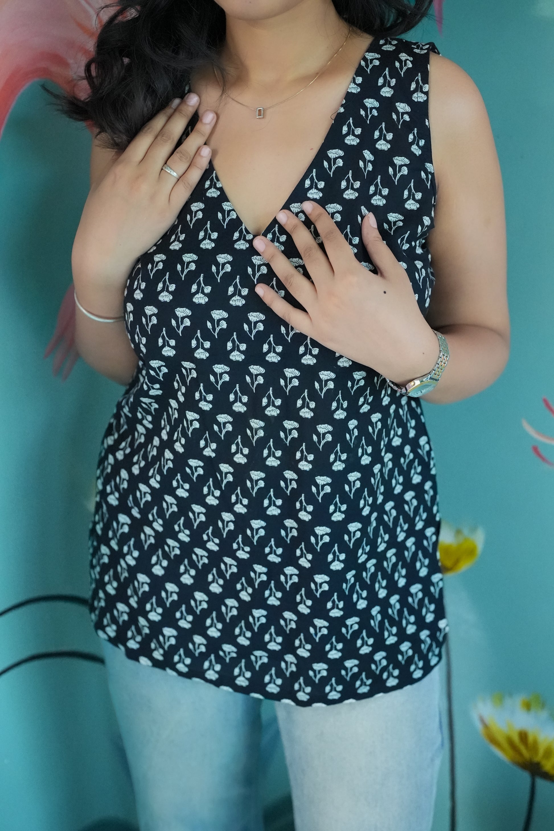 Person wearing a black floral sleeveless top against a blue background Karaa