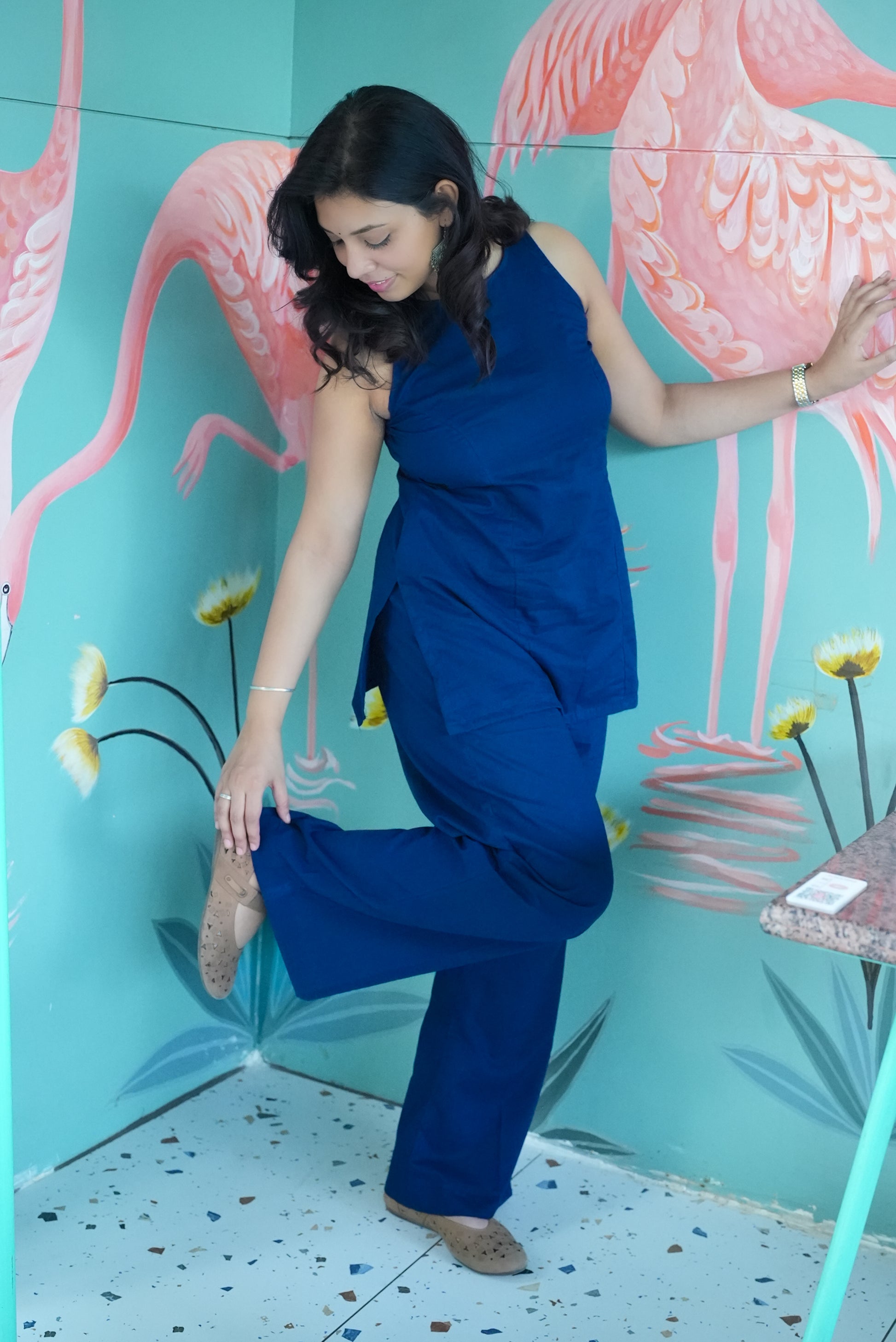 Woman in a blue outfit posing in front of a flamingo mural. Karaa