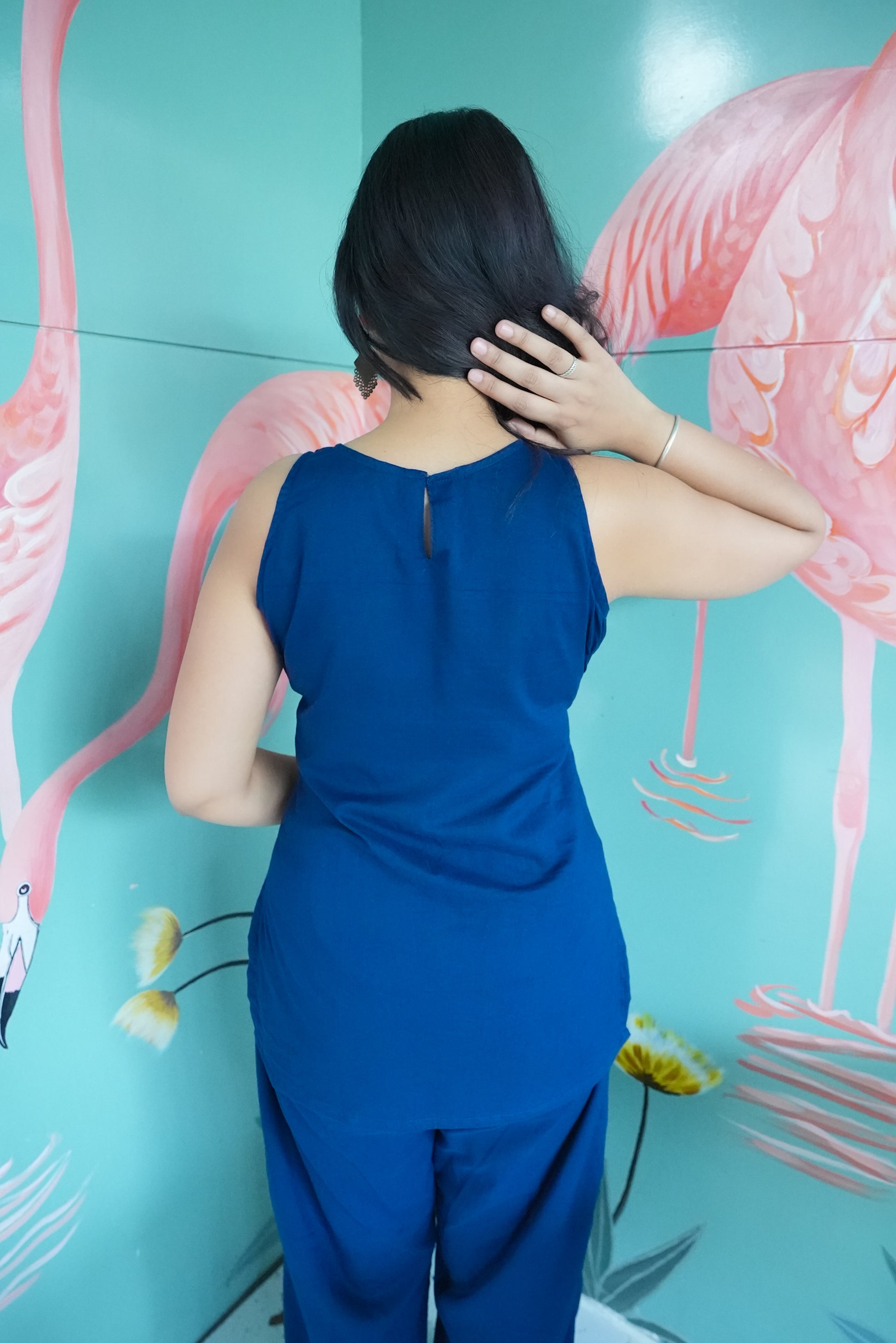 Person wearing a blue outfit standing in front of a flamingo mural. Karaa