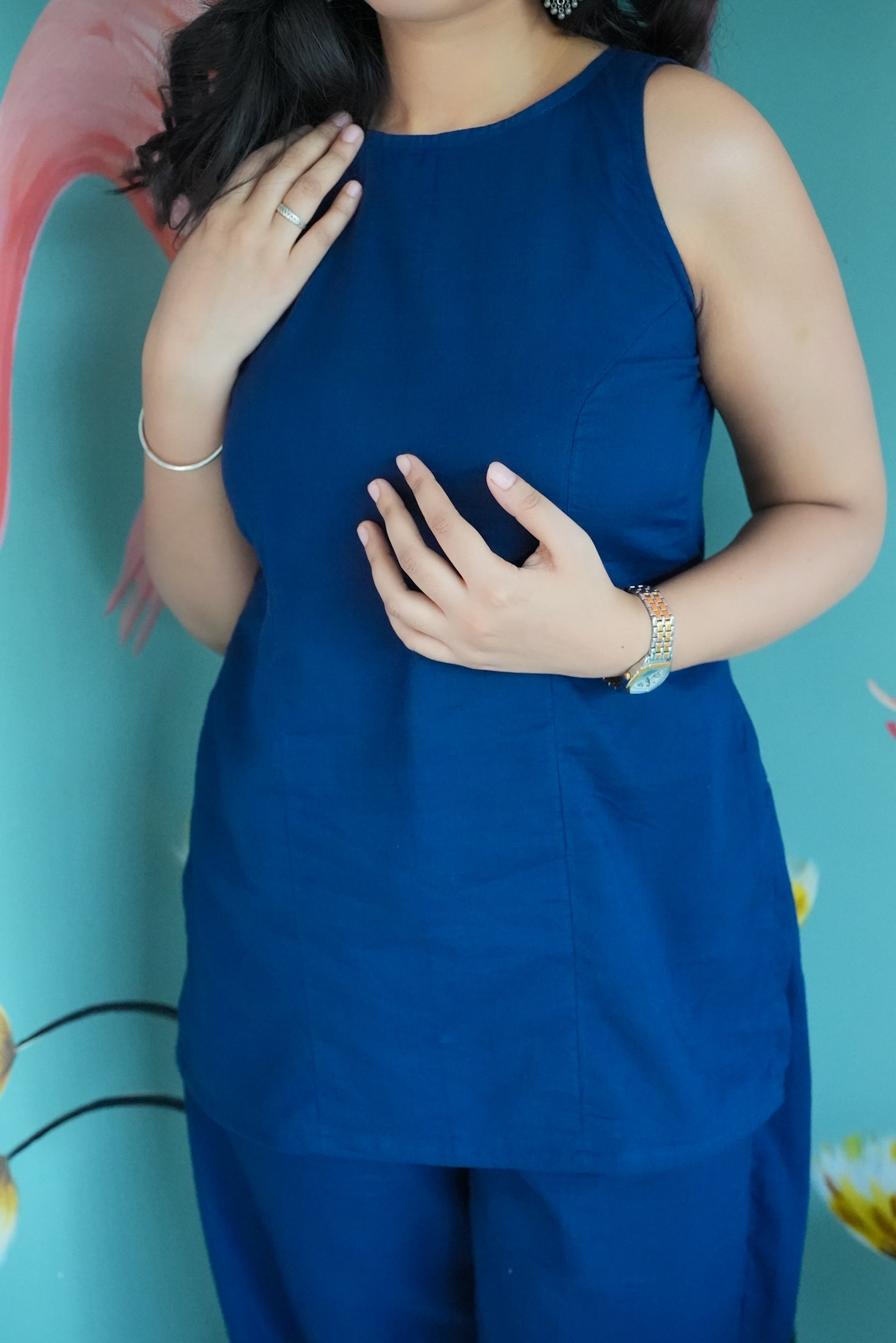 Person wearing a blue sleeveless top and pants against a light blue background Karaa