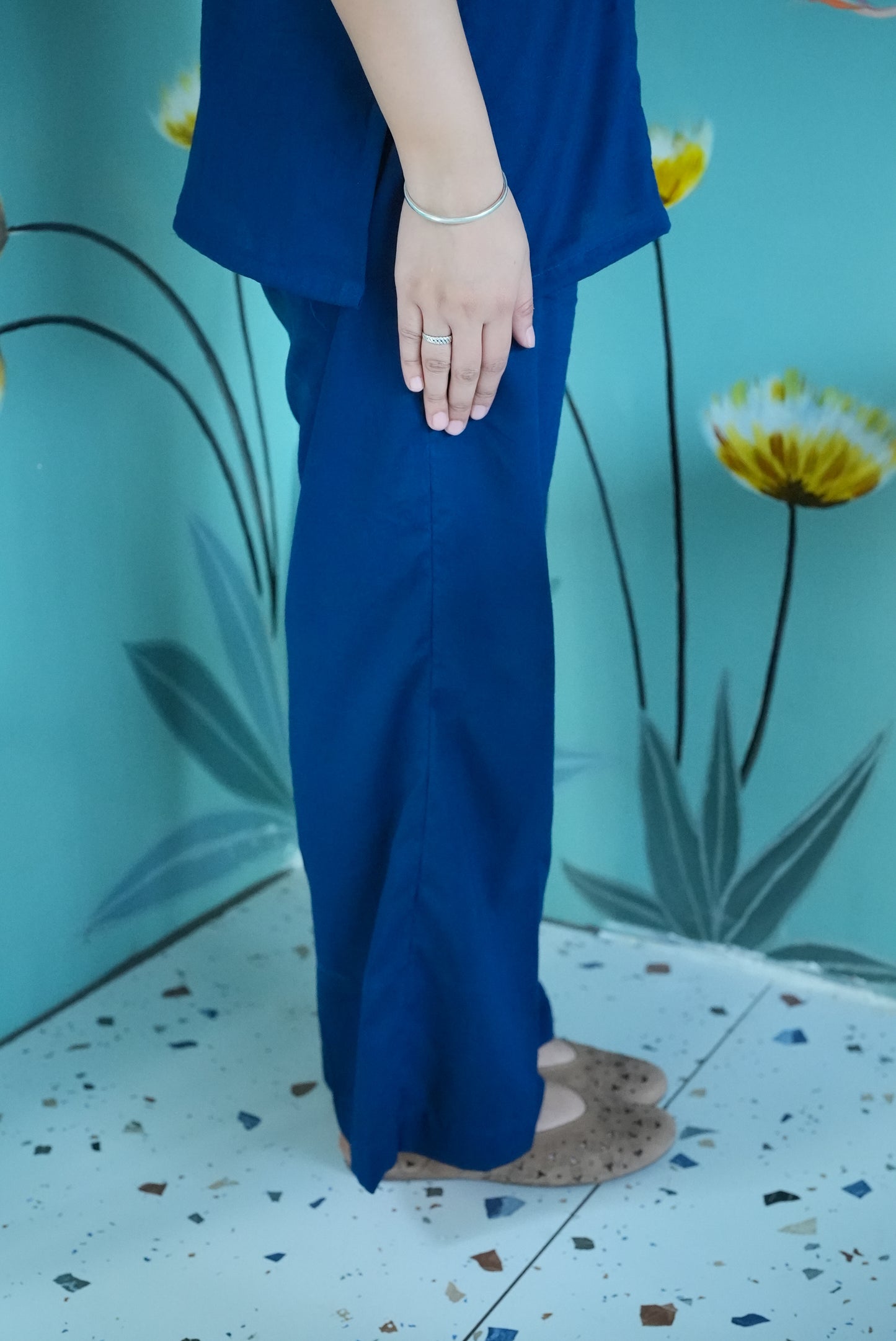Person wearing a blue outfit standing against a floral background Karaa