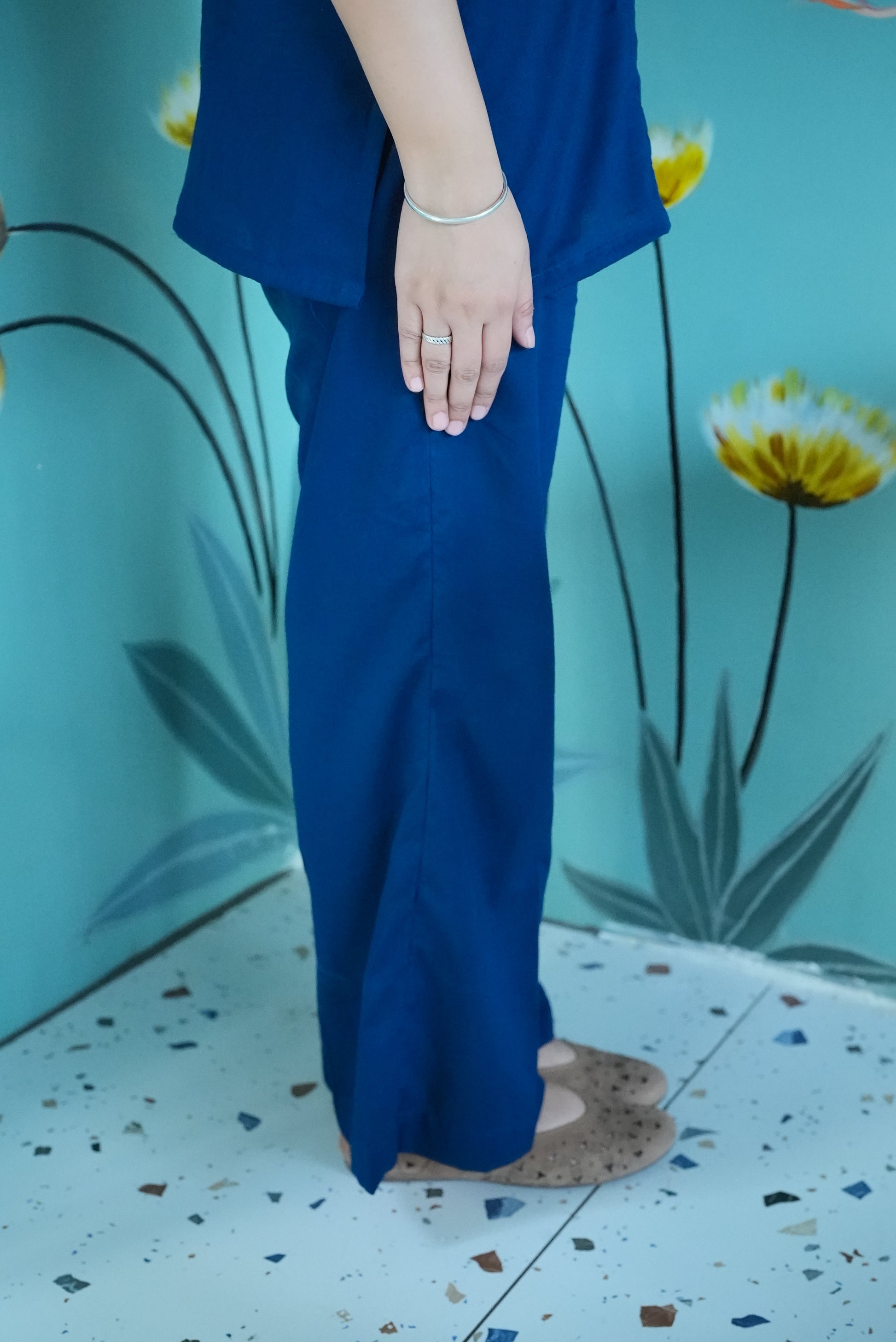 Person wearing a blue outfit standing against a floral background Karaa