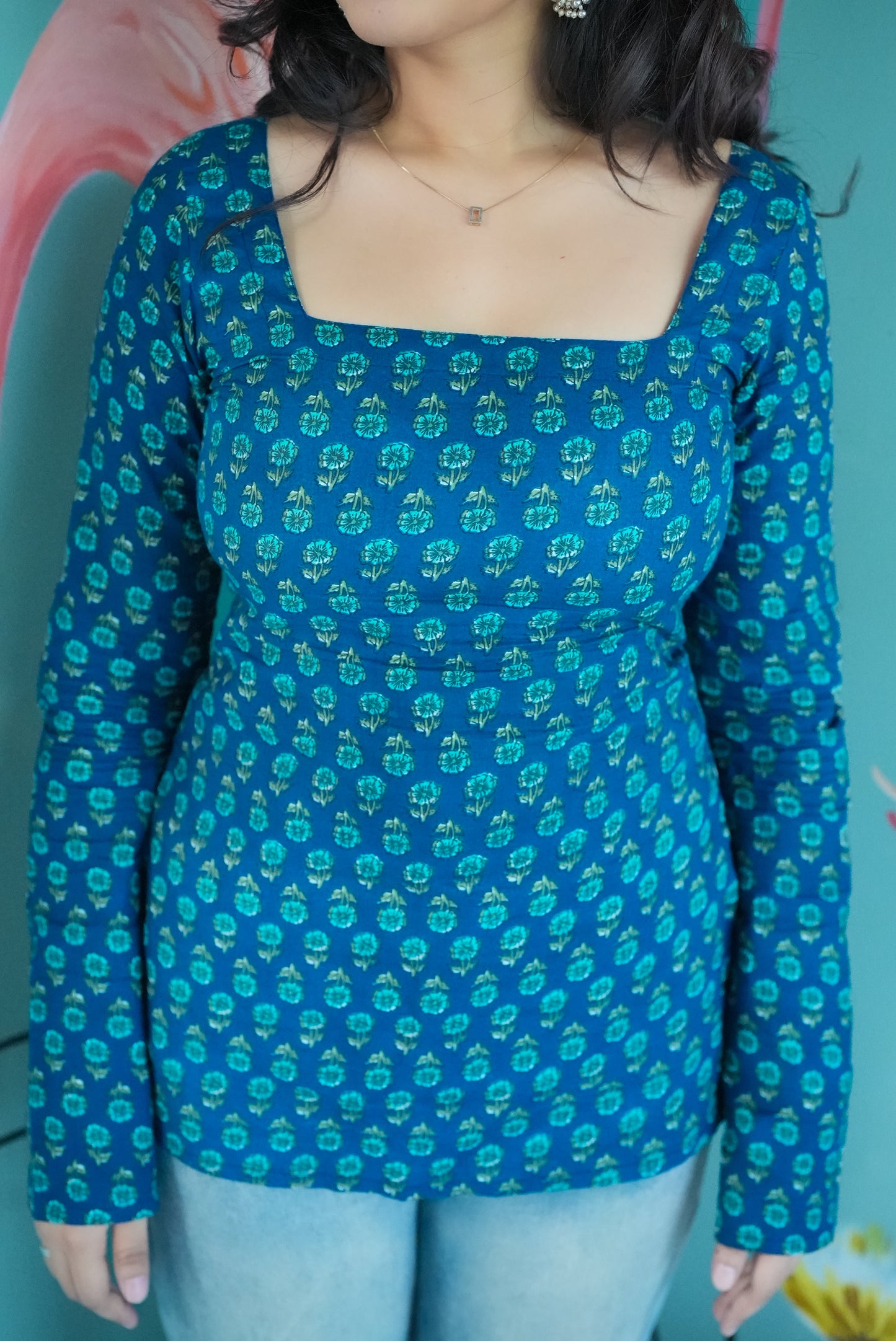 Person wearing a blue floral long-sleeve top against a blue background Karaa
