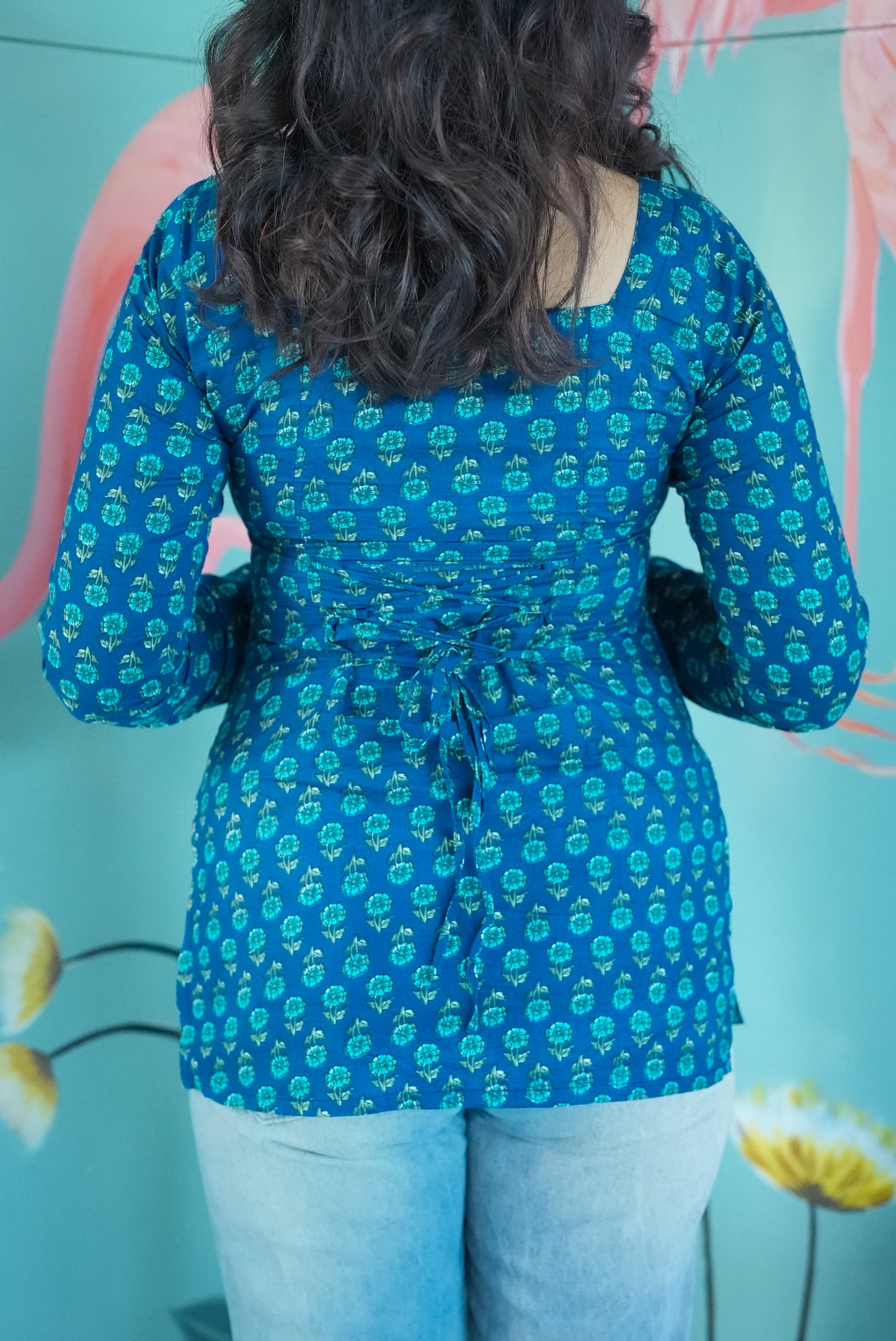 Person wearing a blue floral patterned shirt with a blurred background Karaa