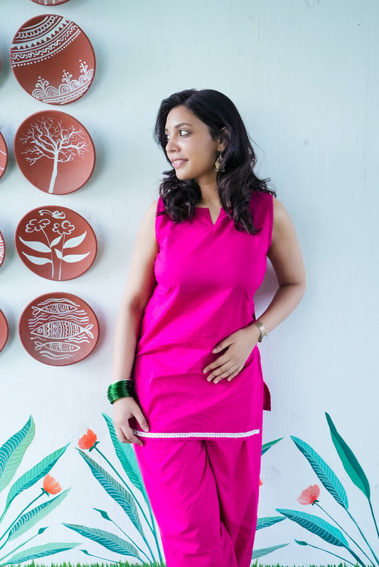 Woman in a pink outfit standing against a wall with decorative plates and floral patterns. Karaa