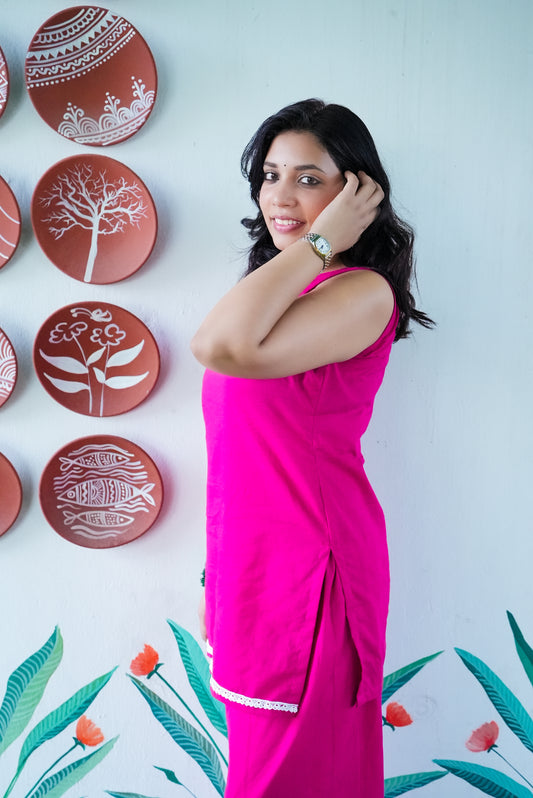 Woman in a pink outfit posing in front of decorative plates on a wall with floral designs. Karaa