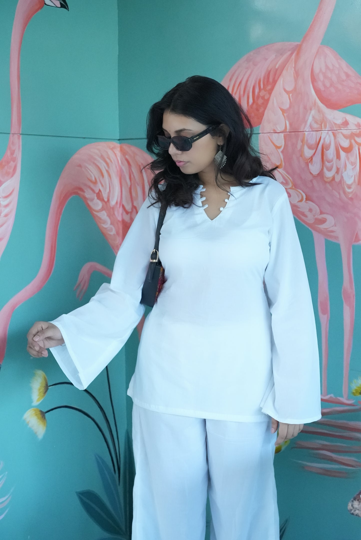 Woman in a white outfit standing in front of a flamingo mural. Karaa