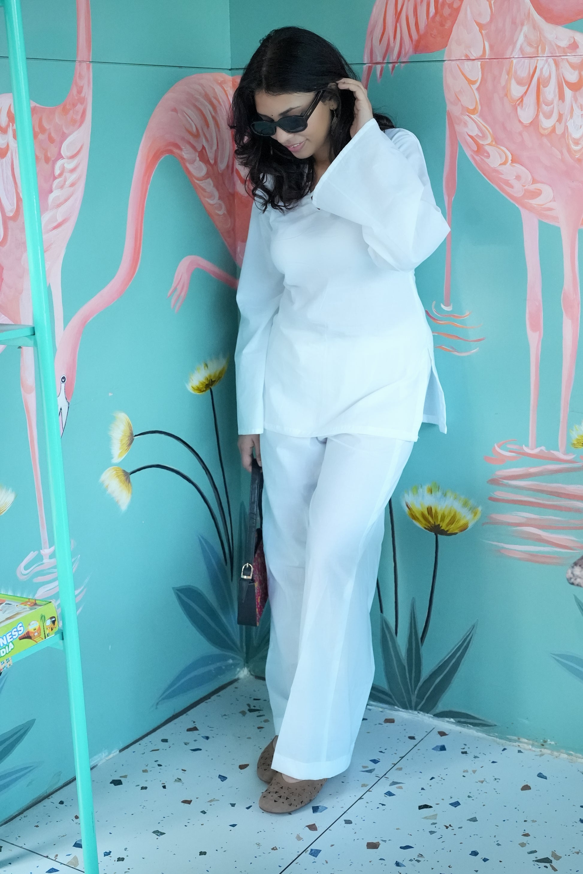 Woman in a white outfit standing in front of a colorful flamingo mural. Karaa