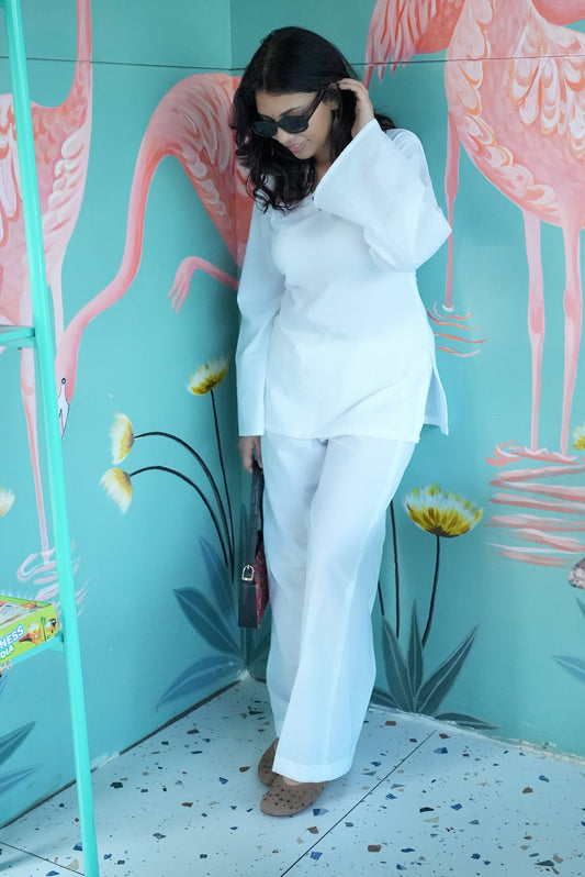 Woman in a white outfit standing in front of a colorful flamingo mural. Karaa