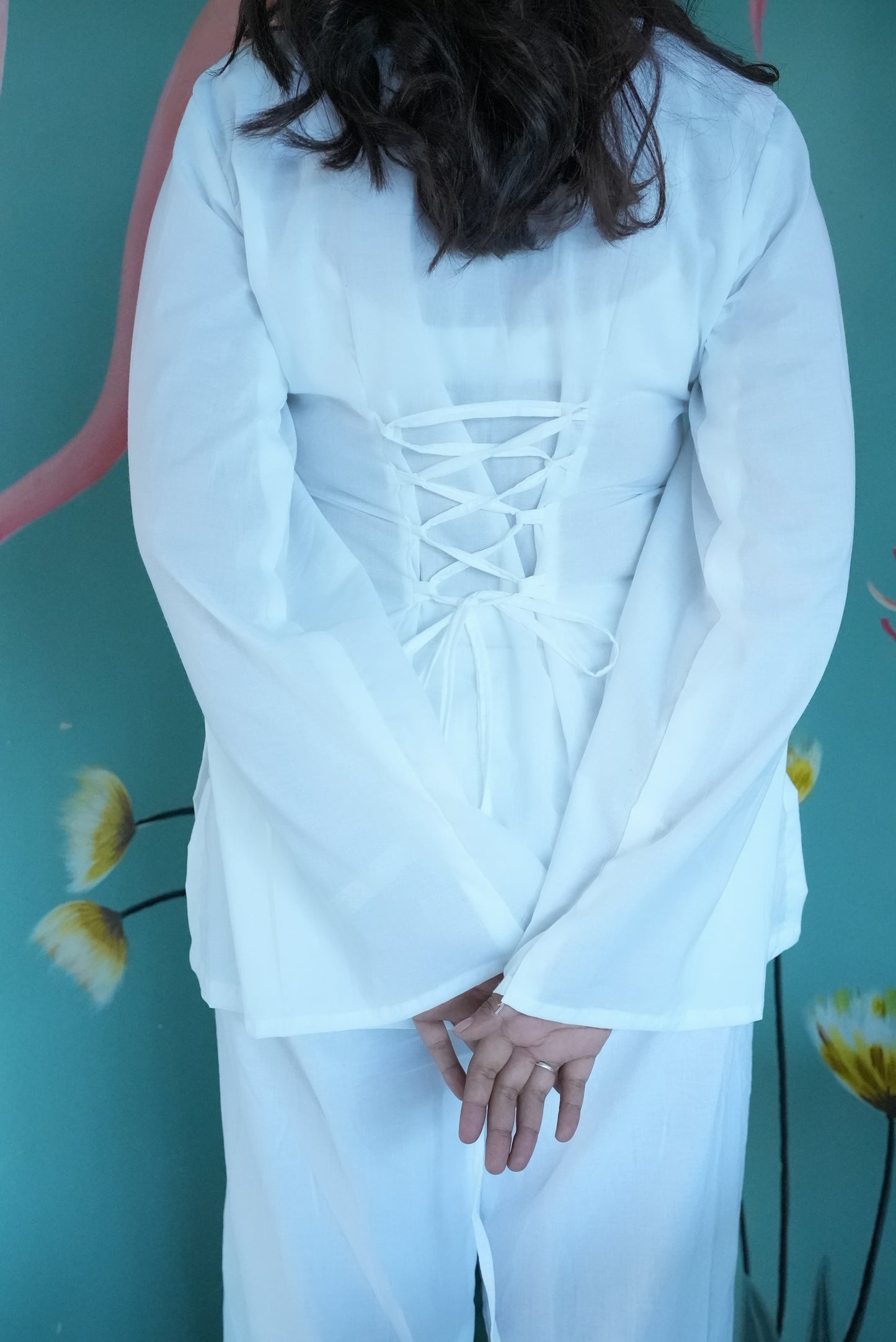 Person wearing a white outfit with intricate back design against a teal background  Karaa